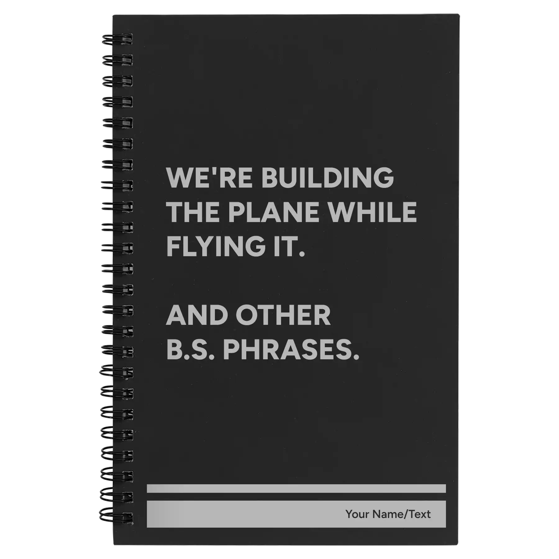 Small black spiral notebook laser etched with 'We're Building The Plane While Flying It. And Other B.S. Phrases' design