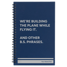 Small blue spiral notebook laser etched with 'We're Building The Plane While Flying It. And Other B.S. Phrases' design